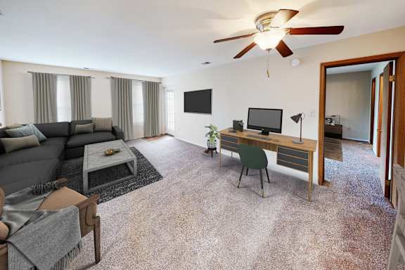 A living room with a grey sofa, a desk with a computer, and a ceiling fan.
