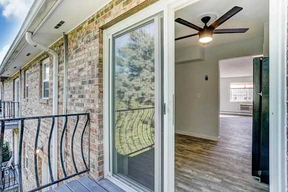 A balcony with a black railing and a glass door leading to a room with a ceiling fan.