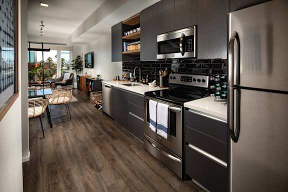 A modern kitchen with a stainless steel refrigerator and wooden flooring.