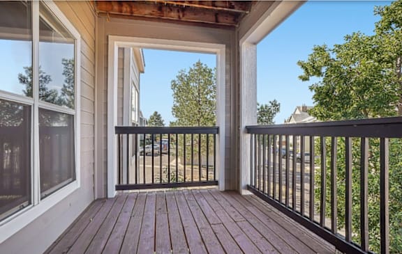 A wooden deck with a black railing and a view of the street.