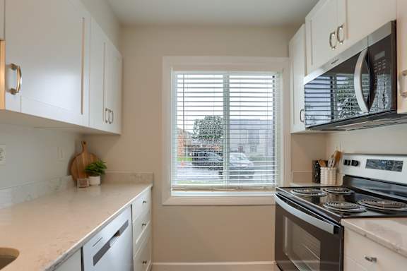 A kitchen with white cabinets and a window with blinds.