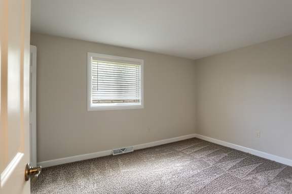 A room with a carpeted floor and a window with blinds.