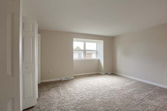 A room with a carpeted floor and a window letting in light.