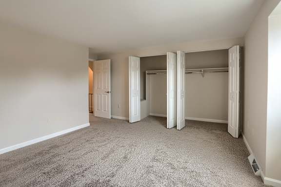 A room with carpeted floor and white walls with a doorway leading to another room.