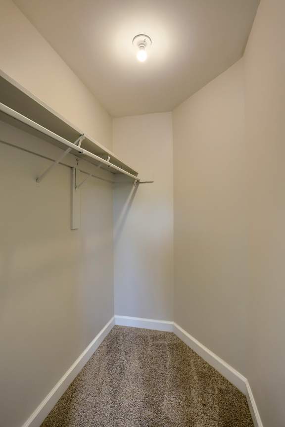 A white wall with a grey carpet and a white ceiling with a light on.