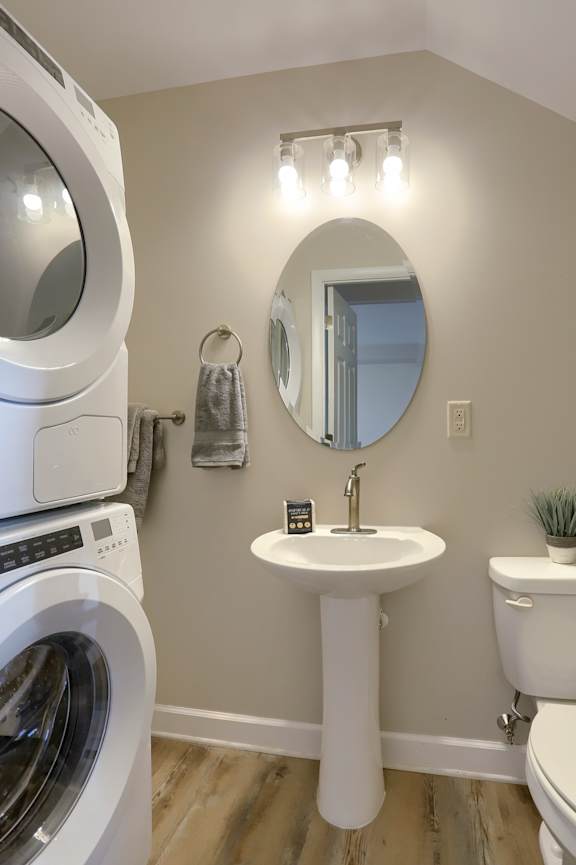 A white washing machine sits next to a white pedestal sink in a small bathroom.