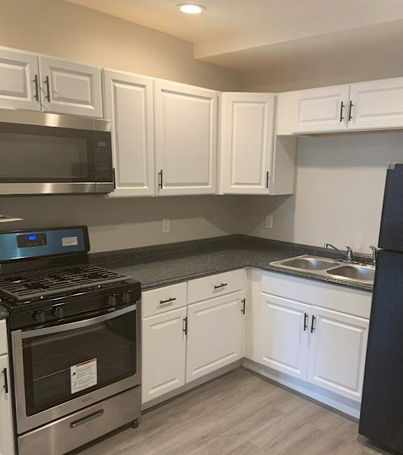 A kitchen with white cabinets and a black refrigerator.