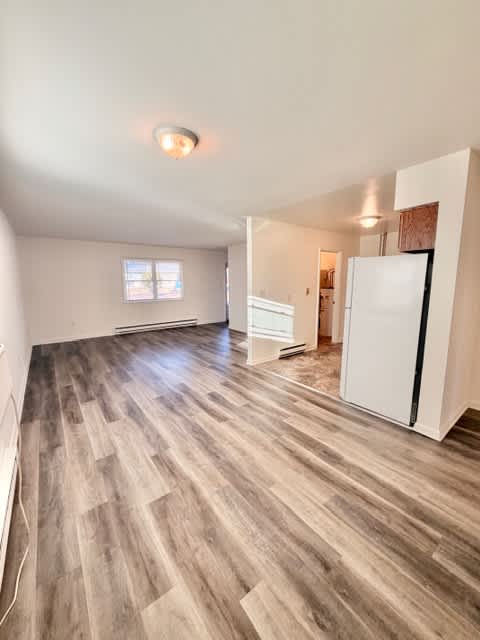 A room with wooden flooring and a white refrigerator.