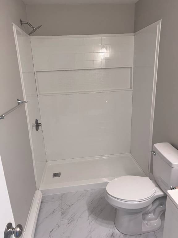 A white toilet in a small bathroom with a walk-in shower.