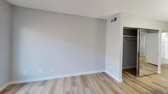 A room with a wooden floor and a white wall with a doorway leading to another room.