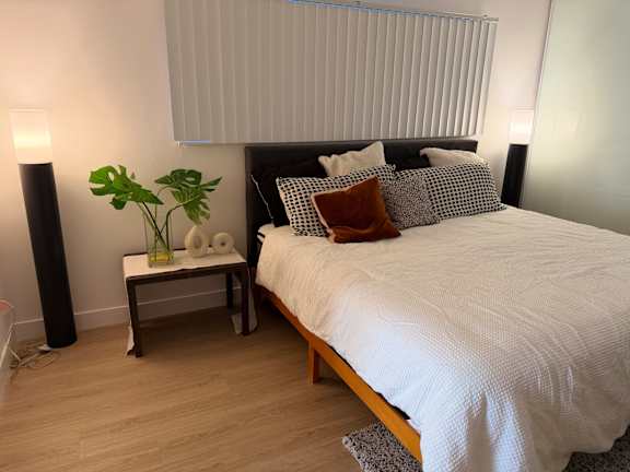 A bedroom with a large bed and a plant on a small table.