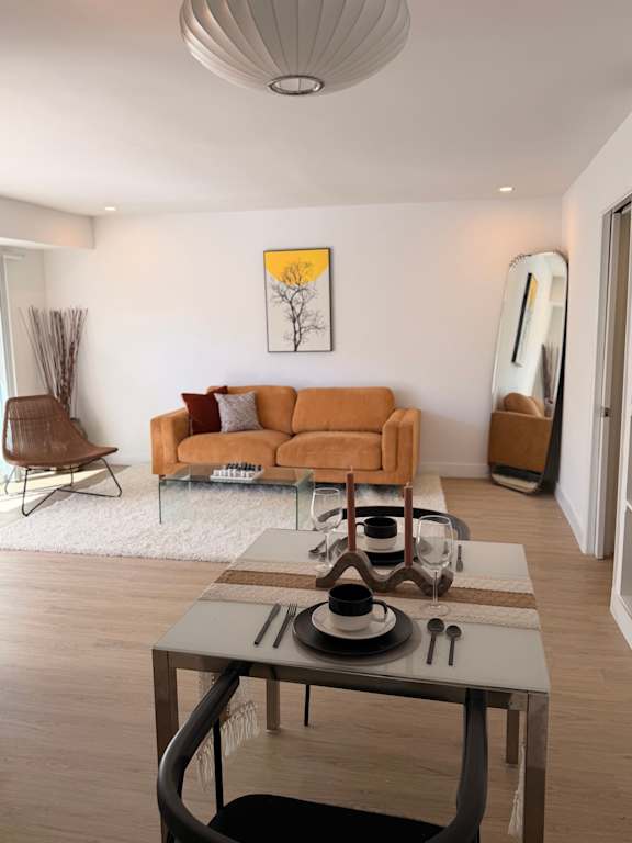 A modern living room with a brown sofa, a glass coffee table, and a painting on the wall.