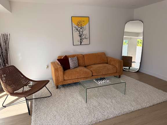 A living room with a brown couch, a chair, and a painting on the wall.