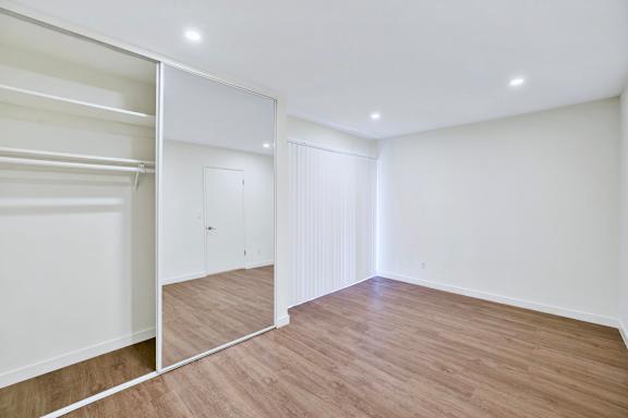 A white closet with a mirror and a wooden floor.