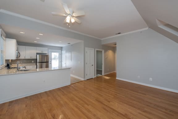 an empty living room with a kitchen and a ceiling fan