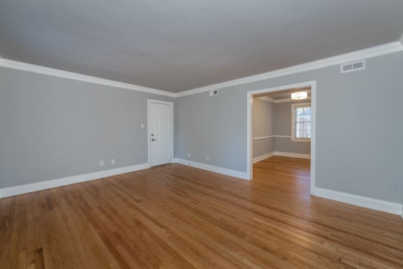 an empty living room with wooden floors and a door into a hallway