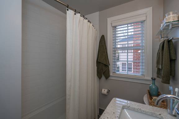 A bathroom with a white shower curtain and a window with blinds.