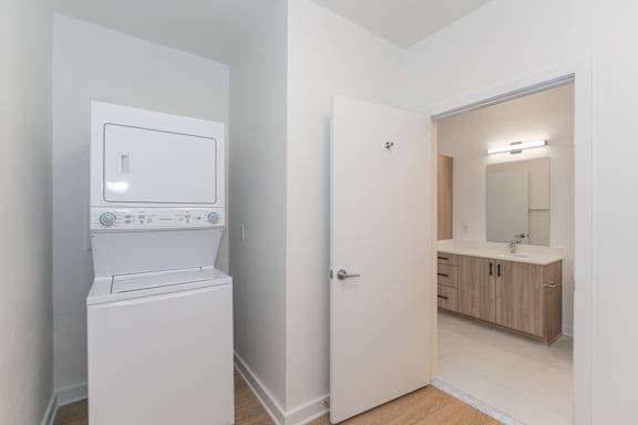A white washing machine in a small room with a bathroom in the background.