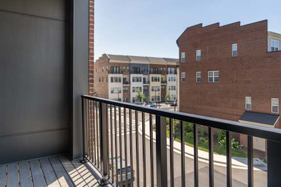 A balcony with a black railing overlooks a street with buildings.