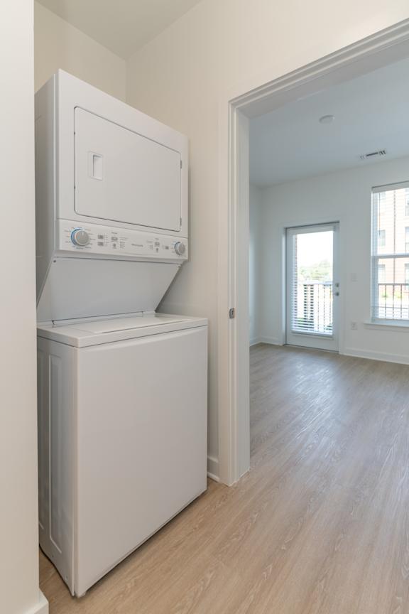 A white dishwasher and dryer stacked on top of each other in a room with light wood flooring.