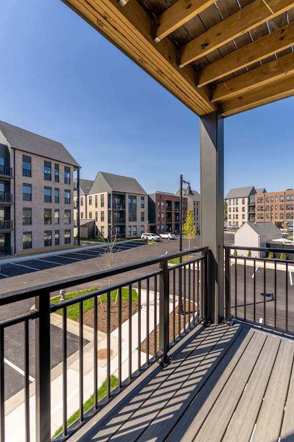 A balcony with a wooden railing overlooks a street with buildings on either side.