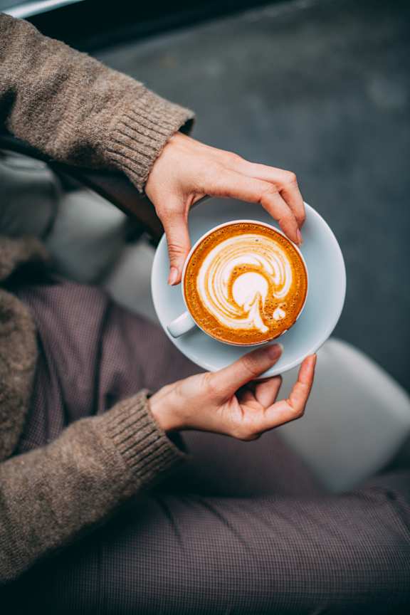 A person is holding a cup of coffee with a latte art design on top.