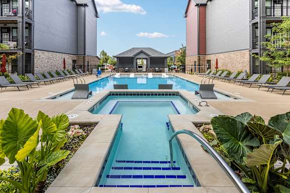 A large outdoor swimming pool surrounded by lounge chairs and plants.