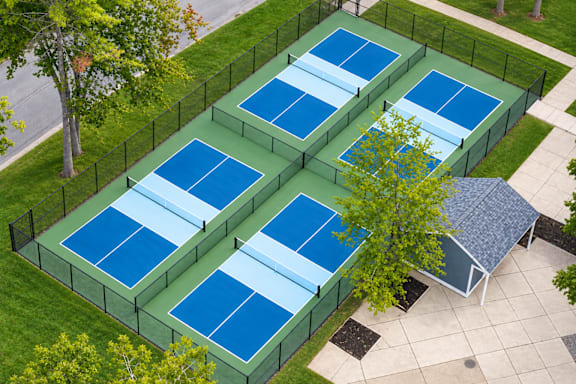 A tennis court is surrounded by a fence and has a small pavilion.