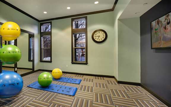 A room with a clock on the wall and exercise balls on the floor.