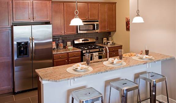 A kitchen with a refrigerator, stove, and bar stools. at Pennsauken Golf Course Villas, PENNSAUKEN, NJ, 08109