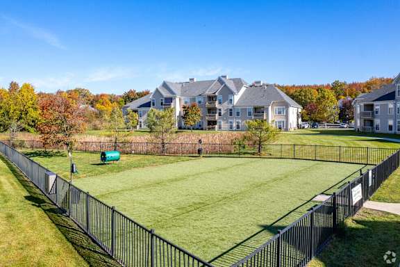 A large grassy field with a fence and apartment buildings in the background.