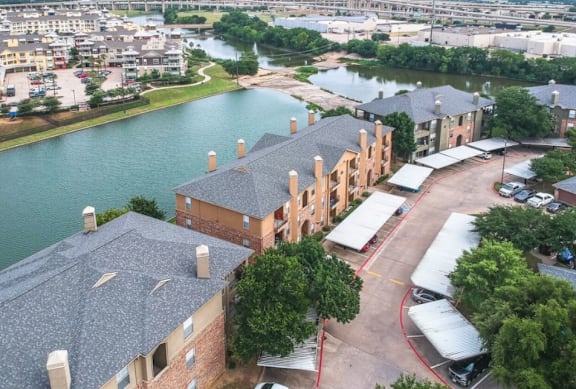 A large building with a grey roof is surrounded by a parking lot and a river.