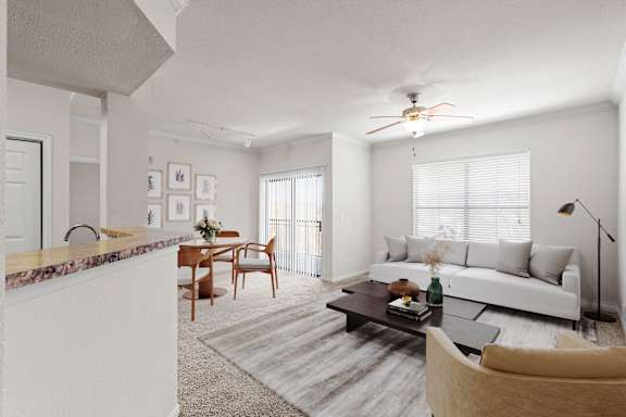 A living room with a ceiling fan, large windows and a dining area.
