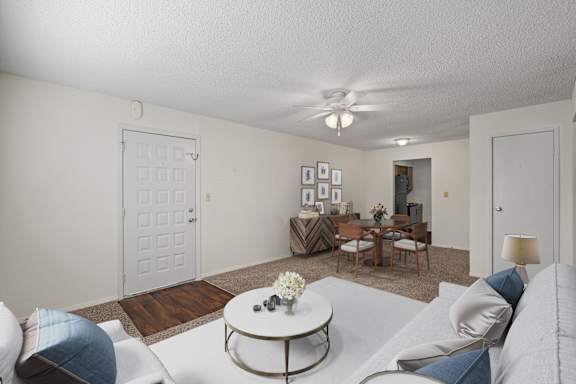A spacious living room with a dining area, ceiling fan, and hallway closet.