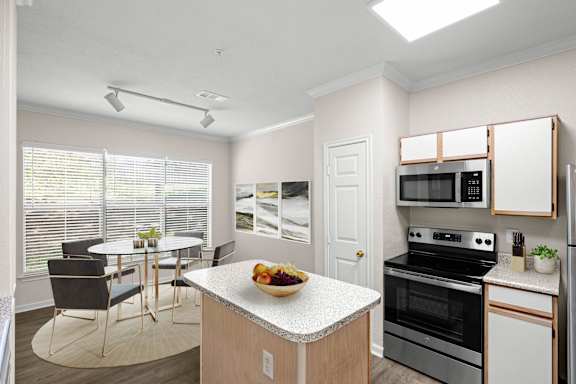 A kitchen with white oak cabinets, stainless steel appliances, track lighting and a kitchen island.