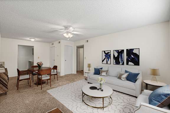 A spacious living room with a dining area, ceiling fan, and hallway closet.
