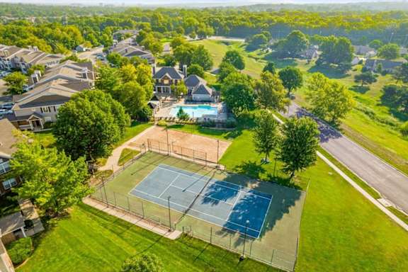 A tennis court is surrounded by a green lawn and trees.