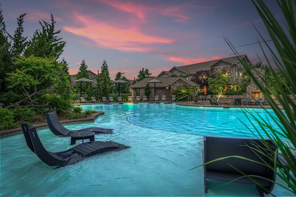 A pool with lounge chairs and a house in the background during sunset. at Stonepost Crossing Apartments, Overland Park
