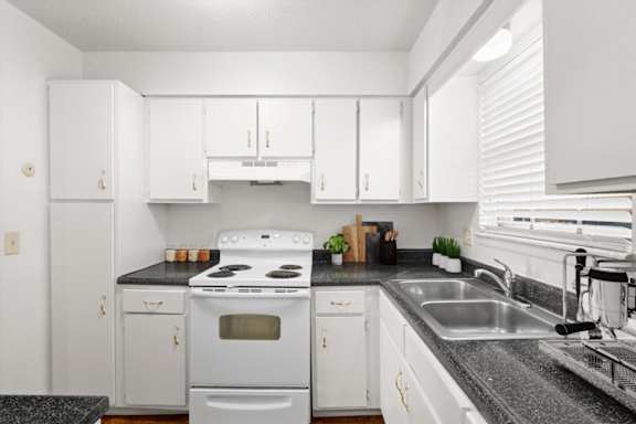 A white kitchen with a black countertop and a stove top oven.