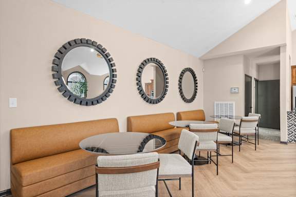 A living room with a brown sofa, a glass table, and three round mirrors on the wall.