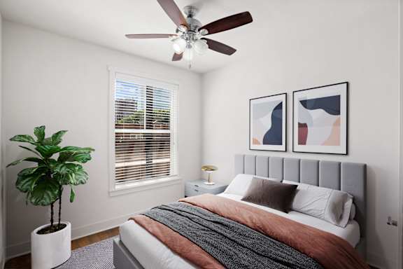 A bedroom with a bed, a ceiling fan, and a potted plant.