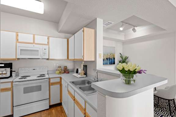 A kitchen with grey countertops, white oak cabinets, white appliances and track lighting.