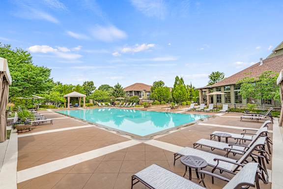 A large swimming pool surrounded by lounge chairs and trees.