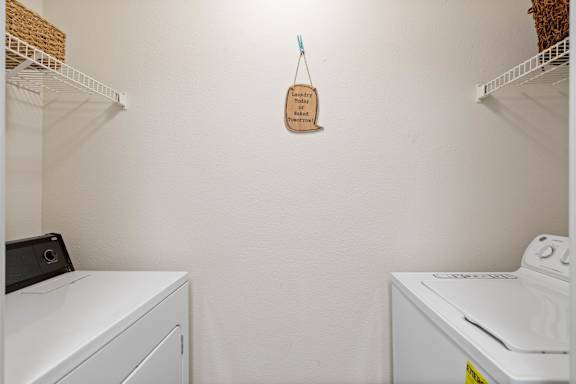 A laundry room with full size washer & dryer, and two wire rack shelves.