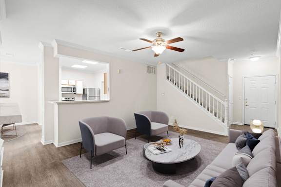 A living room with a ceiling fan and a staircase.