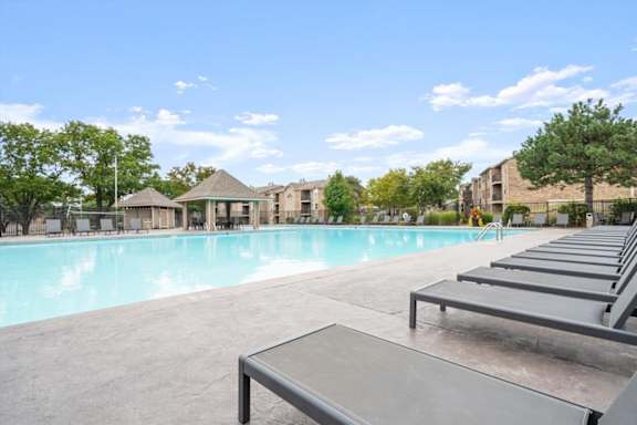 A swimming pool with sun loungers and a pavilion in the background.