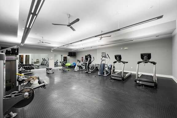 Spacious fitness center at West 39th Street Apartments featuring treadmills, ellipticals, recumbent bikes, free weights, and large wall mirrors at West 39th Street Apartments, Kansas City, 64111