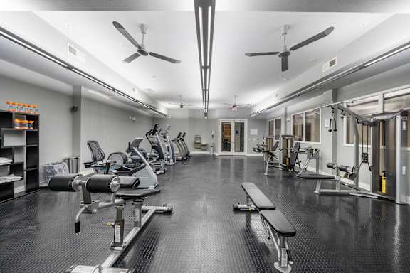 Fully-equipped gym at West 39th Street Apartments with workout benches, cable machines, cardio stations, and ceiling fans at West 39th Street Apartments, Kansas City, Missouri