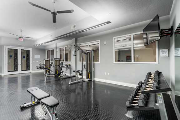 Free weights, strength machines, and mounted TV in fitness center at West 39th Street Apartments at West 39th Street Apartments, Kansas City, MO, 64111