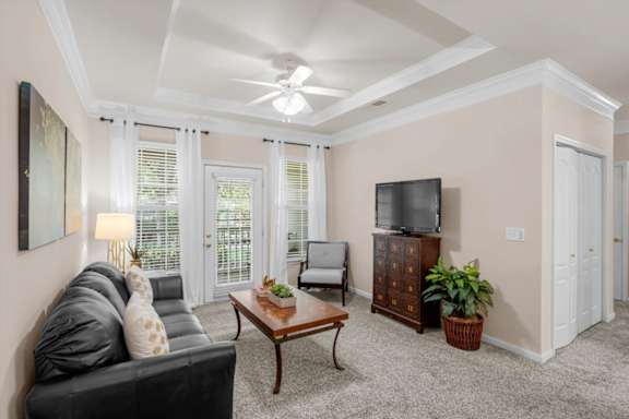 A living room with a black couch, a wooden coffee table, a flat screen TV, and a ceiling fan.
